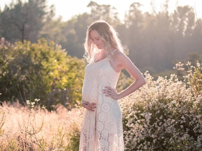 A pregnant woman standing in a sunlit field